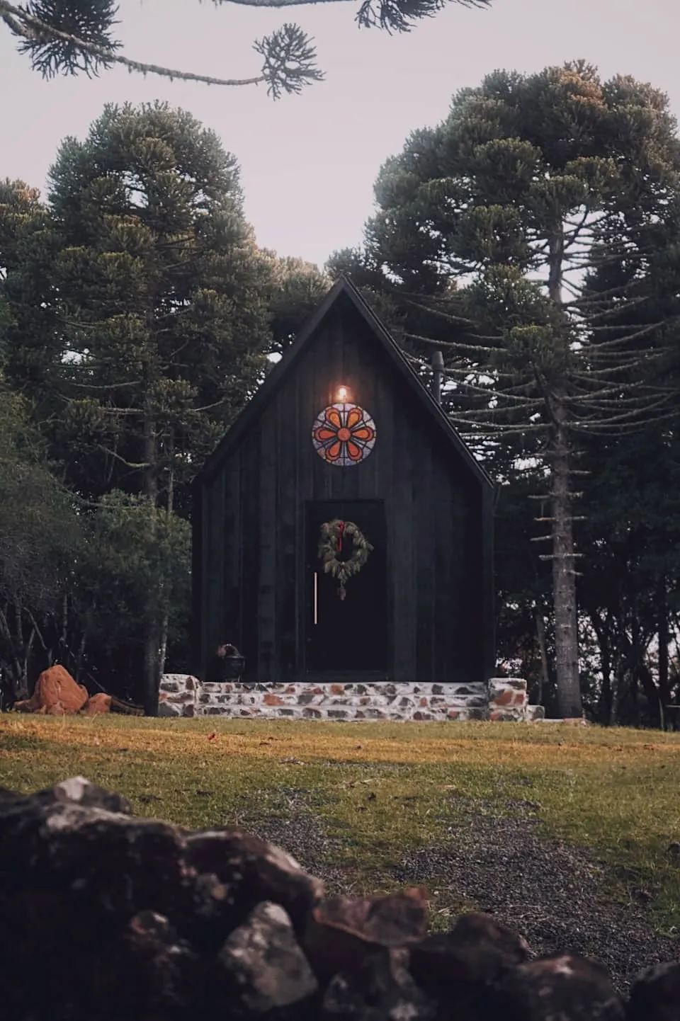 A fachada em A da cabana, com guirlanda na porta, entre as araucárias