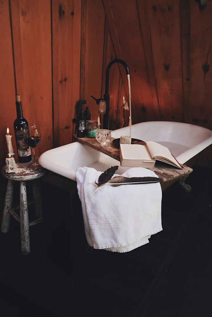 Banheira com pés, vinho, vela e livro junto à parede de madeira