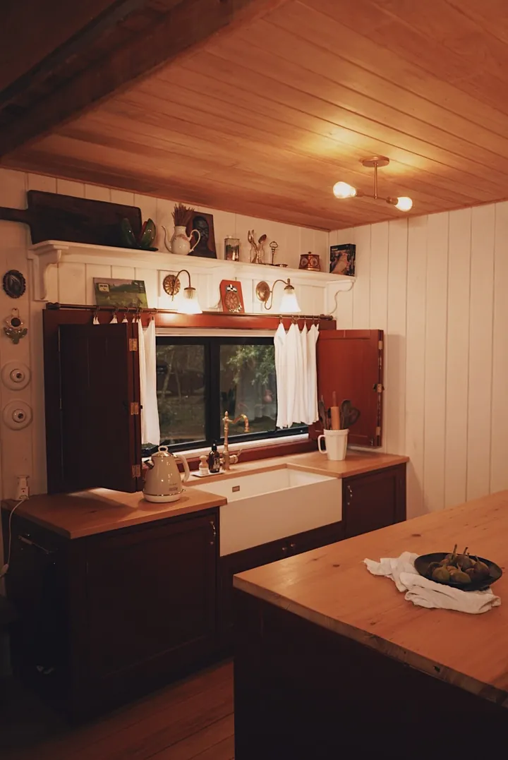 Cozinha com bancada de madeira, cuba de louça e cortinas brancas