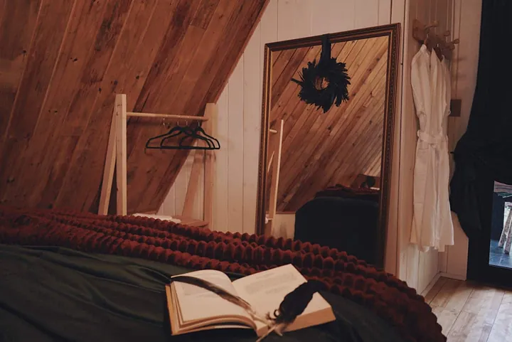 Cama com manta cor de ferrugem e um livro aberto, diante do espelho