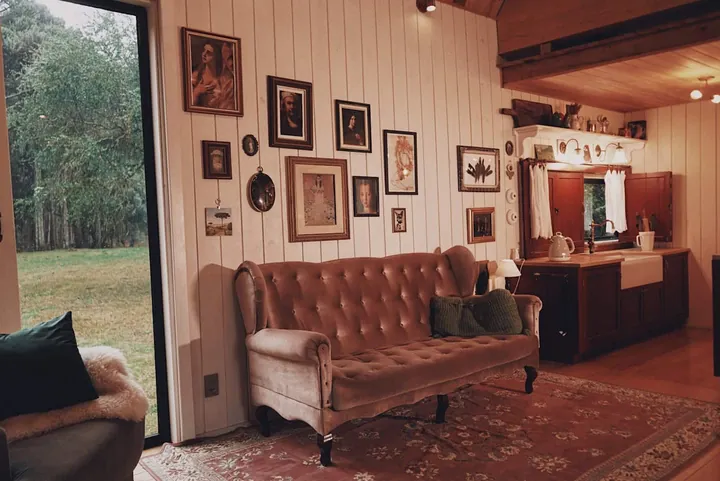 Sala com sofá capitonê, quadros na parede e a porta aberta para o campo